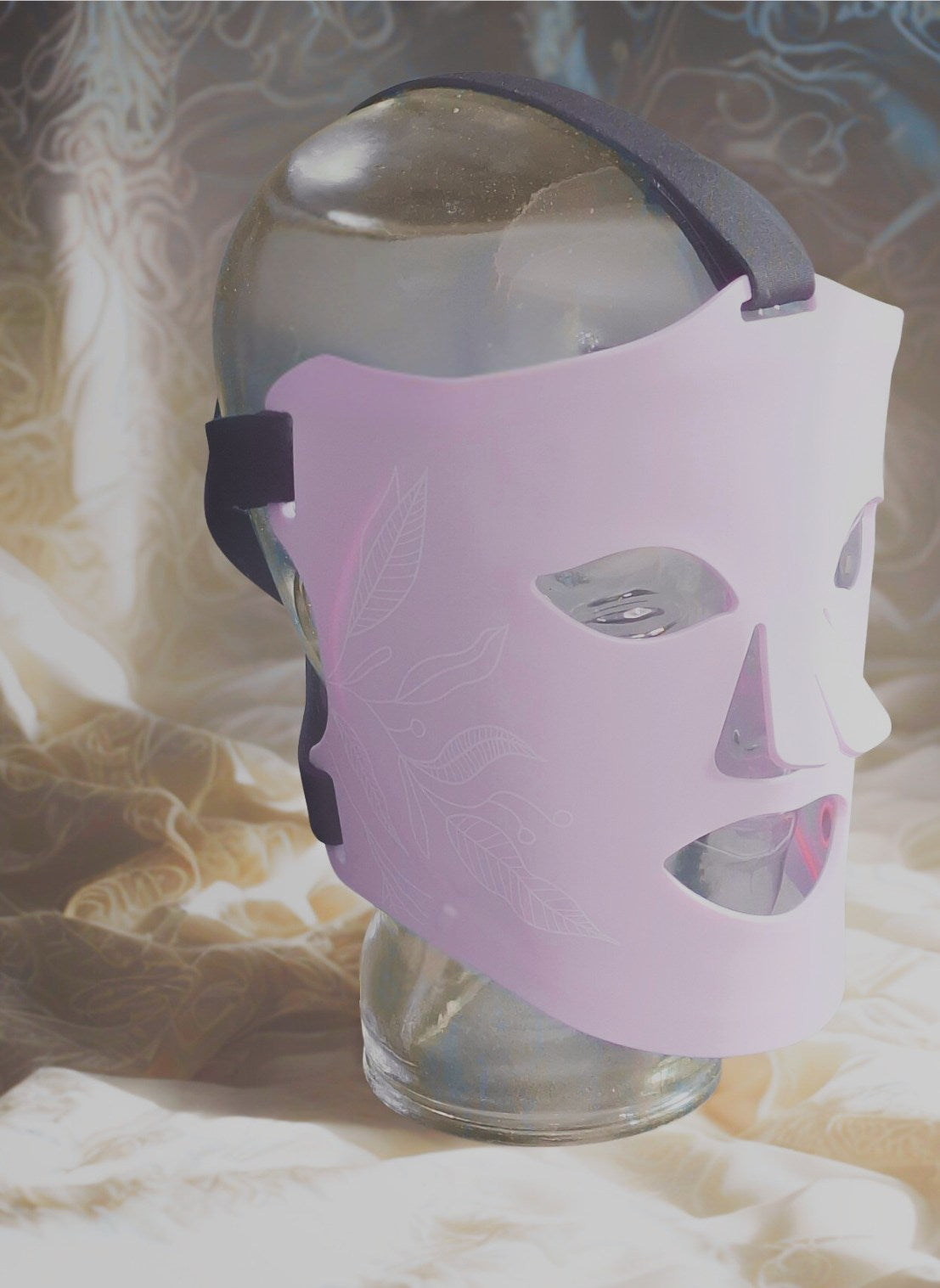 La rêveuse Masque LED ONËRA parme présenté sur tête en verre, appareil de luminothérapie visage au design doux et élégant pour soins esthétiques visage haut de gamme à la maison 8 longueurs d'ondes active collagène