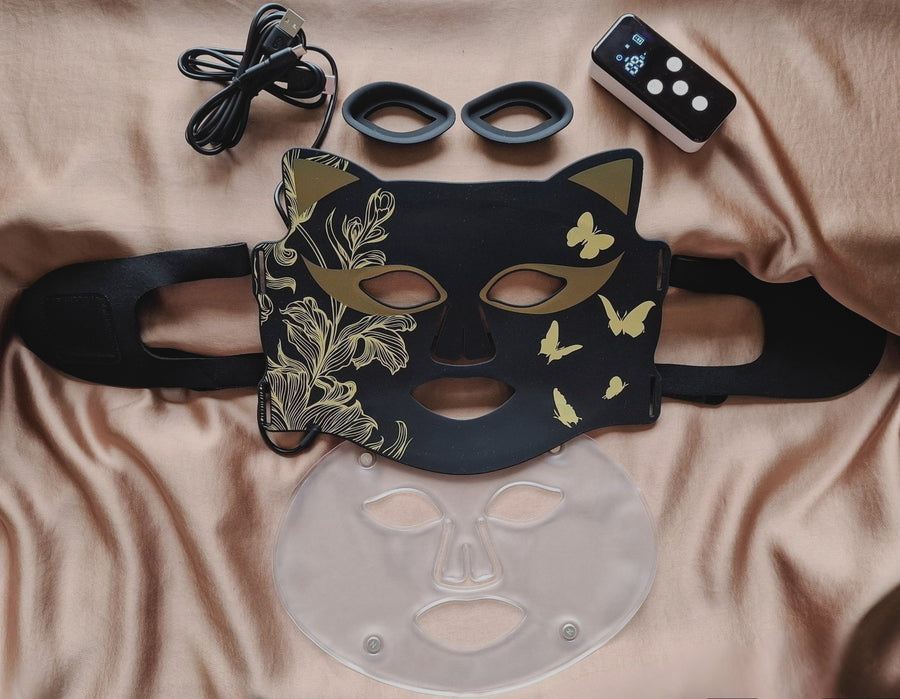 glamour Masque LED ONËRA Glam Cat noir et or, appareil de luminothérapie visage avec télécommande et accessoires pour routine anti-âge et éclat de la peau à domicile, univers glamour sur fond élégant satin